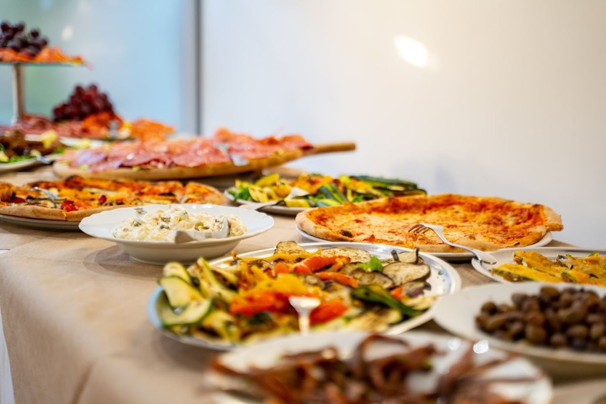 Tavola imbandita con pizze, salumi, verdure grigliate, olive e frutta
