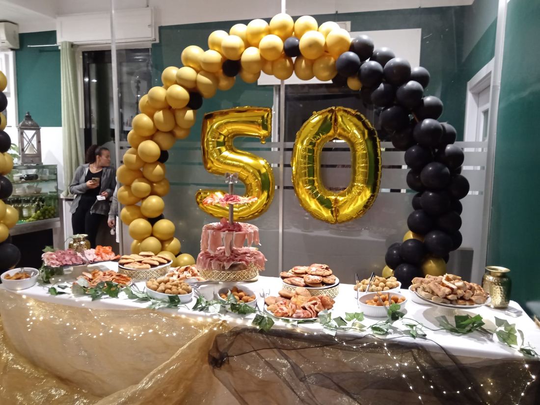 Sala allestita per un compleanno: arco di palloncini oro e nero, numeri 50 e buffet